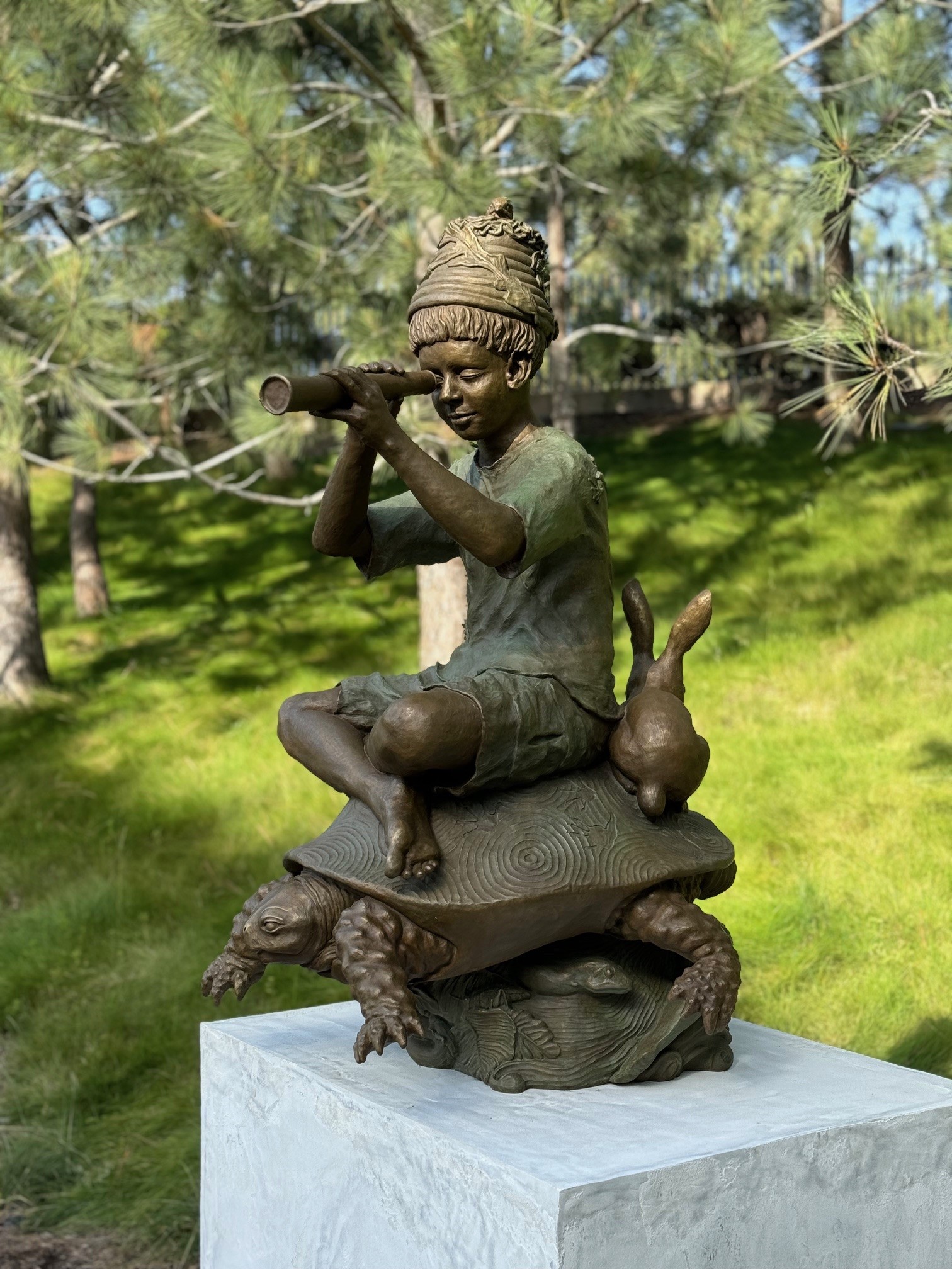 Sculpture of a boy sitting on a turtle looking through a spyglass - sculpture in Civic Center Park